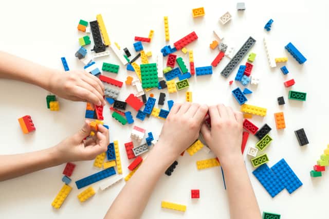 Children hands play with colorful lego blocks on white table.
