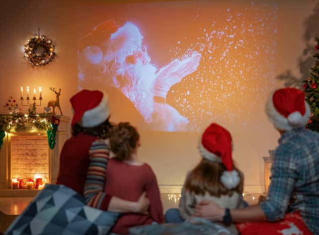 People having fun near tree indoors. Loving family watching holiday movies at home. Mother, father and daughters spending time together.