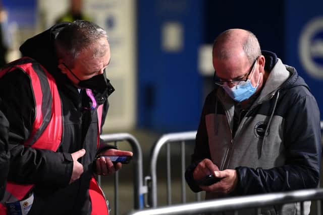A supporter has his Covid-19 status checked as he arrives ahead of the English Premier League football match between Brighton and Hove Albion and Wolverhampton Wanderers at the American Express Community Stadium. (Photo by GLYN KIRK/AFP via Getty Images)