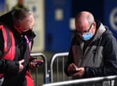A supporter has his Covid-19 status checked as he arrives ahead of the English Premier League football match between Brighton and Hove Albion and Wolverhampton Wanderers at the American Express Community Stadium. (Photo by GLYN KIRK/AFP via Getty Images)
