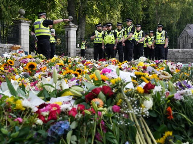 Police officers arrive at the gates of Balmoral in Scotland where flowers and tributes have been laid by members of the public following the death of Queen Elizabeth II. The Queen's coffin will be transported on a six-hour journey from Balmoral to the Palace of Holyroodhouse in Edinburgh, where it will lie at rest. Picture date: Sunday September 11, 2022.