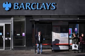 Commuters wait at a bus stop outside a branch of Barclays in London.