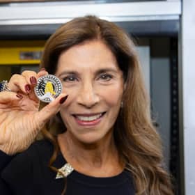 Freddie Mercury's sister, Kashmira Bulsara, holding the new Royal Mint commemorative coin. The design features Mercury mid-performance, his signature, and details like his Live Aid outfit (Photo: Royal Mint)