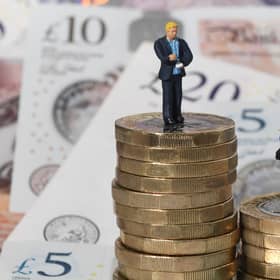 Models of a man and woman stand on a pile of coins and bank notes.