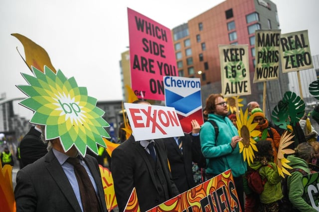 Protesters holding signs of major oil and gas companies are seen outside the entrance to the COP26 site