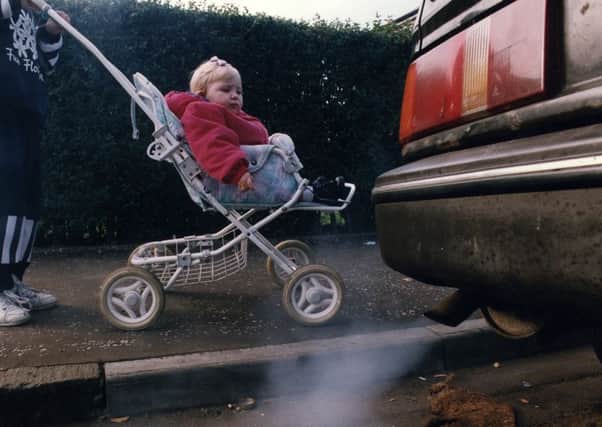 Baby in pushchair beside car exhaust fumes.