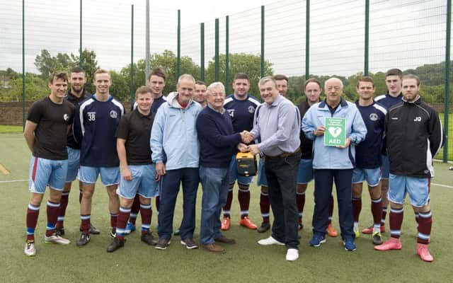 United players look on as Eric hands over the defibrillator to club chairman George Watson.