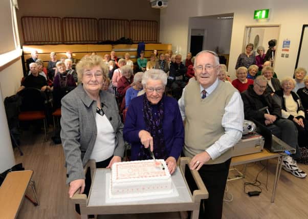 Chris Wilson (centre) cuts her birthday cake with Nora Porteous and Bill Clark of Motherwell Heritage Society.