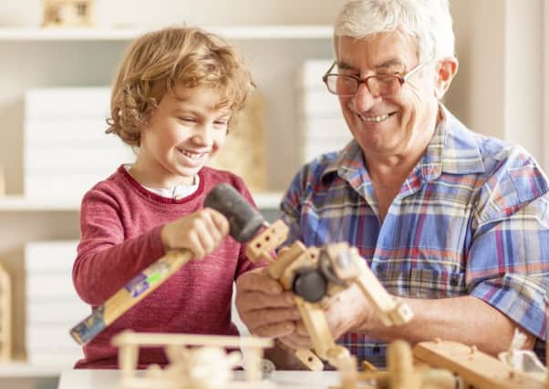 Grandparents are shaping their grandchildrens childhoods by sharing their experiences. A Grandpa and his grandson crafting wooden toys together in a workshop.