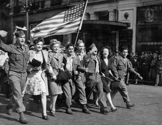 On hearing on radio of the Japanese offer to surrender on 10 August 1945, American soldiers and English girls parade the 'Stars and Stripes' past the famous Criterion restaurant in Piccadilly Circus, London (Photo: IWM)